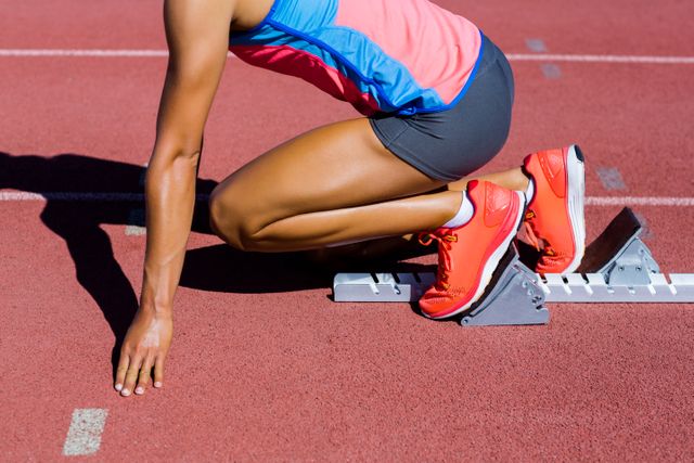 Depicts a female athlete in starting blocks on a running track. Ideal for promoting sports events, fitness training programs, athletic gear, and motivational content about competition and determination. Can be used in articles about athletic training, women's sports, and outdoor fitness activities.