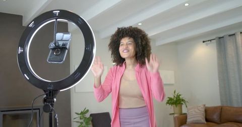 Female creator filming live tutorial with ring light and smartphone in modern living room