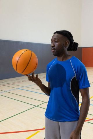 African american athlete balancing basketball on finger in indoor gym