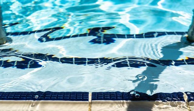 Shimmering turquoise pool water rippling over lane lines and deck edge in sunlight