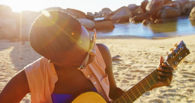 Person playing guitar on sunny beach with rocks in background - Download Free Stock Images Pikwizard.com