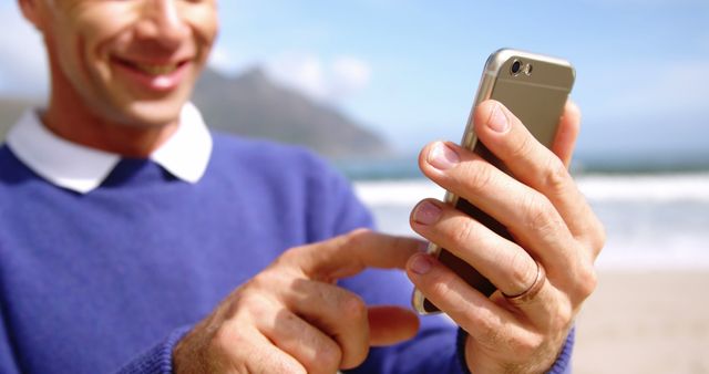 Man holding smartphone smiling by ocean on a sunny day - Download Free Stock Images Pikwizard.com