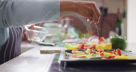 Senior woman sprinkling herbs on colorful vegetable tray with futuristic hud overlay