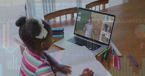 Child watching online lesson while writing in notebook during remote learning at home