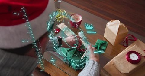 Man in santa hat wrapping gifts at glass table with digital augmented reality hud overlay