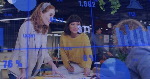 Young professional women collaborating and analyzing digital charts and blueprints at work
