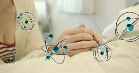 Caregiver holding patient hands with floating atom models symbolizing compassionate healing