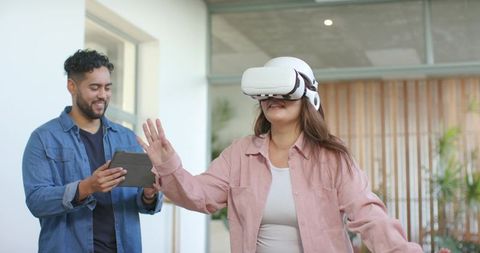 Woman Trying VR Headset While Coworker Monitoring on Tablet in Bright Office