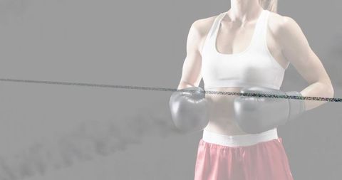 Female boxer wearing gloves and pink shorts in minimalist gray studio with smoke