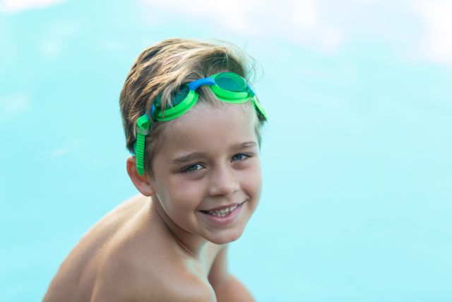 Young boy enjoying time at the pool, wearing green swimming goggles and smiling. Perfect for summer, outdoor activities, and childhood joy themes. Ideal for advertisements, blogs, and articles related to swimming, kids' activities, and family fun.
