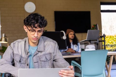 Young asian man working on laptop in bright coworking space with colleague