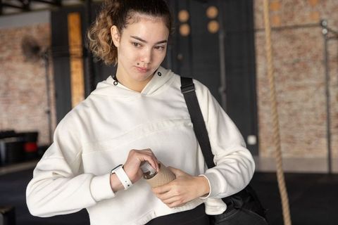 Young woman twisting lid of reusable tumbler after workout in urban gym