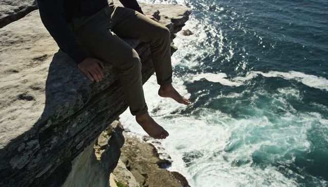 Sitting on cliff edge dangling barefoot over foamy ocean waves coastal adventure lifestyle