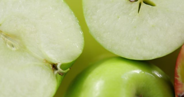 This detailed close-up features green apples, one split in half to reveal its juicy interior and seeds. Perfect for visuals focusing on healthy eating, diet plans, organic produce markets, and vegetarian recipes. Highlight freshness and natural ingredients in any advertisement or blog post about fruits and nutrition.