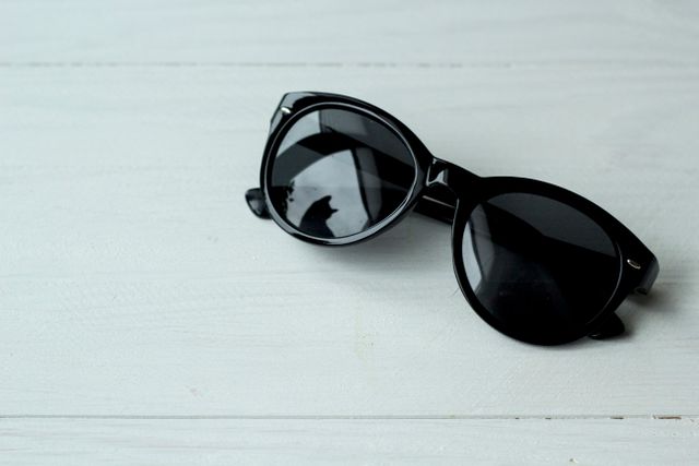This image displays a pair of black sunglasses placed on a white wooden surface. It can be used in articles or advertisements related to fashion trends, summer accessories, or sun protection. Ideal for fashion magazines, online stores selling eyewear, or lifestyle blogs promoting stylish looks.