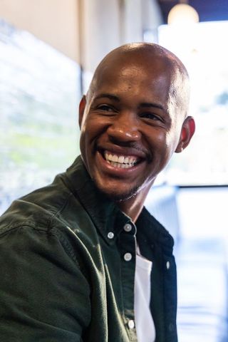 Smiling young man sitting in cafe wearing dark green button-up shirt, casual portrait