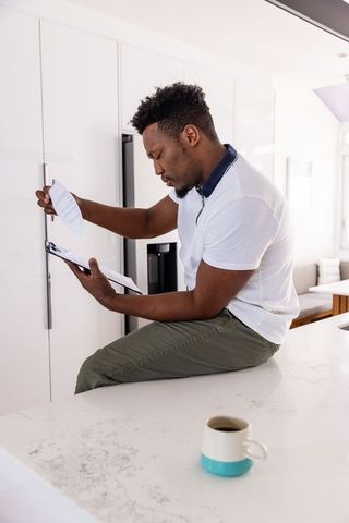 African american man reviewing paperwork on white kitchen counter with coffee