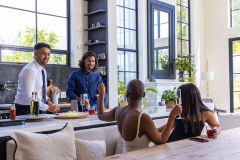 Sunlit friends gathering around modern kitchen island sharing drinks and conversation