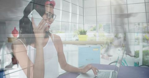 Young professional talking on phone while typing on laptop in bright modern workspace