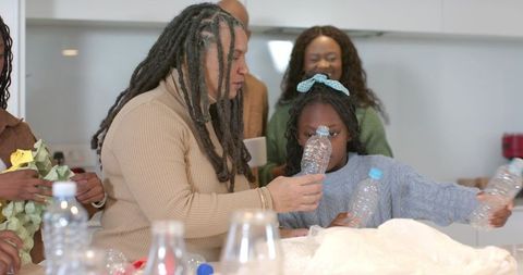 Dreadlocked man passing water bottle to african american child at kitchen counter