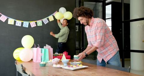Diverse coworkers arranging office baby shower with pastel balloons, cupcakes, gift bags