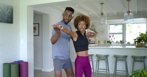 Couple stretching during home workout while trainer guides arm alignment in kitchen