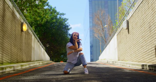 Young woman dancing hip hop on a city street against backdrop of trees and tall buildings. She is wearing a casual outfit consisting of a T-shirt, ripped jeans, and sneakers. Great for use in content around urban lifestyle, modern dance, youth culture, and street fashion.