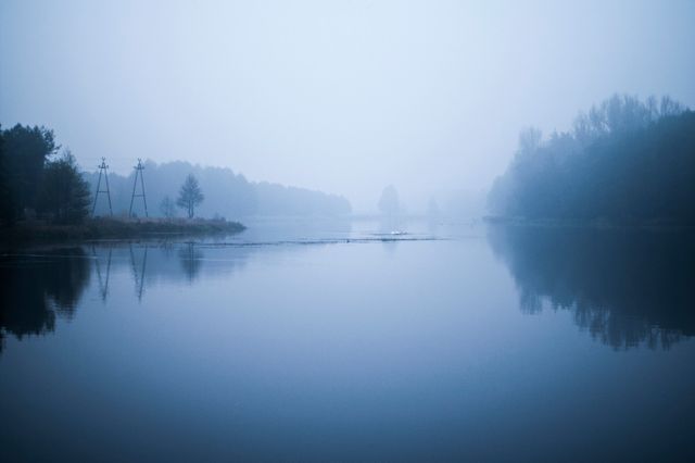 Peaceful misty lake at dawn with still waters reflecting trees, ideal for illustrating tranquility and serenity in nature settings. Perfect for backgrounds in presentations, wallpapers, or nature-focused articles and projects.