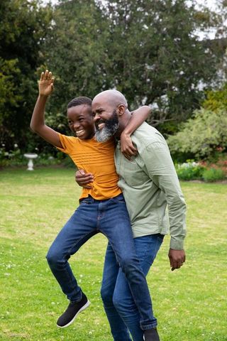 Joyful African American Father and Son Piggybacking in Garden