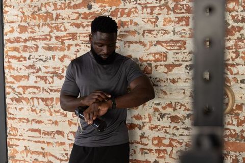 African american athlete checking smartwatch after gym workout holding water bottle against brick wa