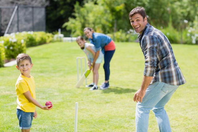 Family having fun playing cricket in backyard on a sunny day, ideal for concepts of family bonding, leisure activities, and outdoor fun. Suitable for advertising summer activities, family events, and promoting outdoor games.