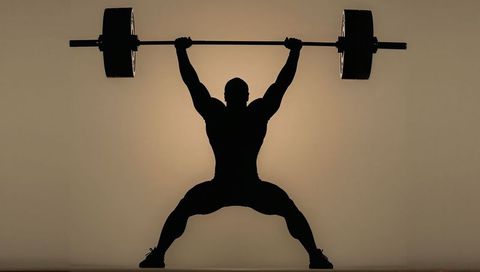 Silhouette weightlifter performing overhead snatch with halo backlight and power pose