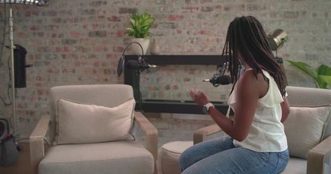 African american woman recording podcast in studio with exposed brick and lounge chairs