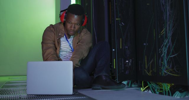 African american male computer technician using laptop working in business server room. digital information storage and communication network technology.