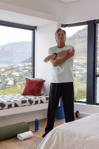Mature man stretching in bedroom during morning home workout with mountain view
