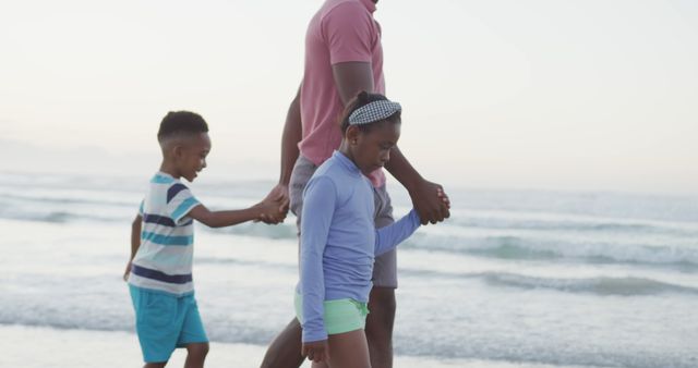 Family enjoying quality time together while walking along the beach at sunset. Ideal for use in promotions or advertisements related to travel, family vacations, parenting, summer activities, and outdoor leisure. Also suitable for illustrating concepts of togetherness, bonding, and happiness.