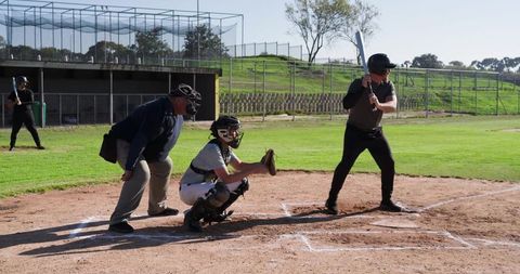 Batter taking stance at home plate with catcher and umpire on sunny baseball diamond