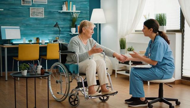 Nurse consulting with senior woman in wheelchair during home care visit and taking notes