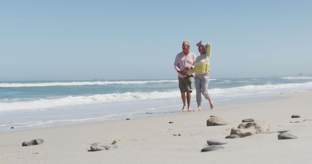 Happy senior caucasian couple holding hands talking to each other while walking on the beach. travel vacation retirement lifestyle