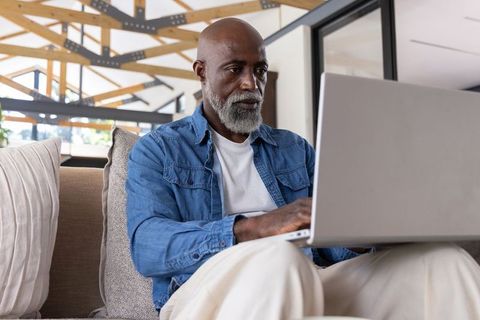 Senior african-american man working on laptop in modern open-plan living room for remote work