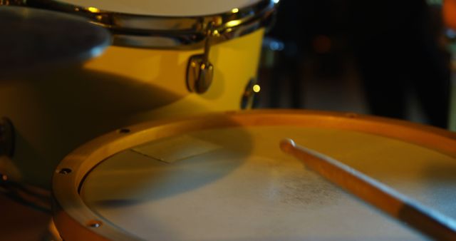 Image showcasing a close-up view of a drum set under low light, ideal for use in content related to music, drumming, bands, and creative arts. Suitable for promotional materials focusing on musical instruments, performance settings, music studios, and artistic environments.