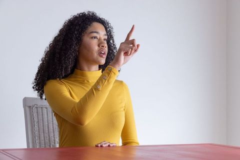 Confident Woman Pointing Upward in Minimalist Home Interior
