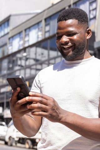 African american man smiling while checking smartphone on busy urban street in daylight