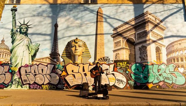 Busker playing guitar against landmark mural with colorful graffiti and urban landmarks