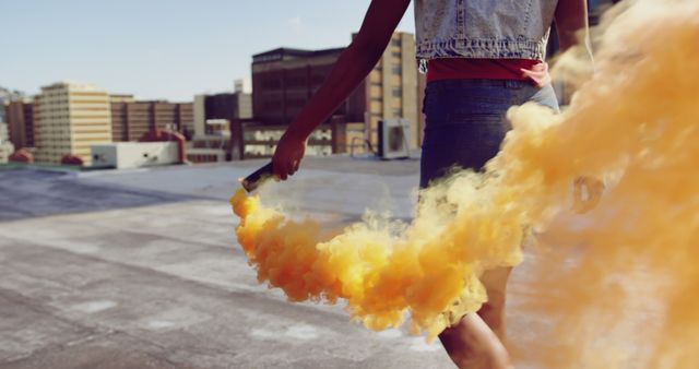 Woman holding smoke bomb on rooftop with urban backdrop. The mix of yellow smoke and urban environment can be useful for advertising campaigns, social media, and creative projects promoting fun, adventure, innovation, and the urban lifestyle.