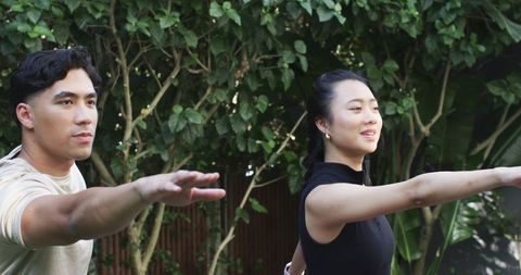 Asian duo stretching arms outdoors for balance and wellness in backyard garden practice