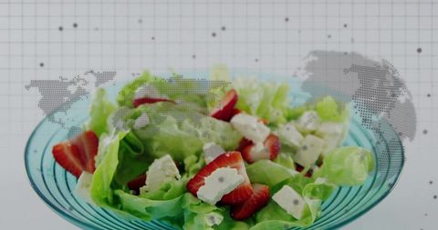 Strawberry feta salad in turquoise bowl with dotted world map backdrop