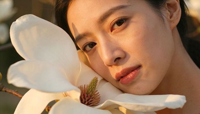 Asian woman resting cheek against magnolia blossom, basking golden hour closeup portrait