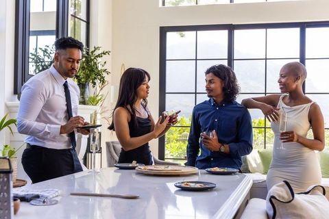 Diverse friends socializing in modern bright kitchen by white island wearing cocktail attire
