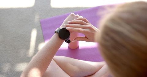 Woman adjusting smartwatch on yoga mat with water bottle